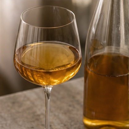 Amber skin-contact wine in a glass beside its bottle